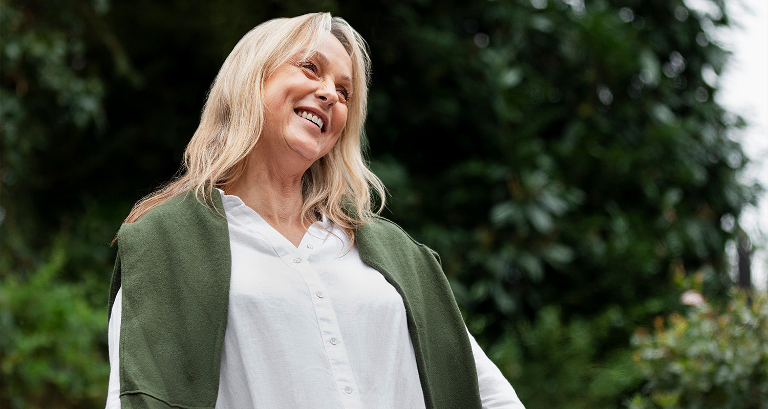 Lachende Frau steht entspannt im Grünen und genießt die Natur