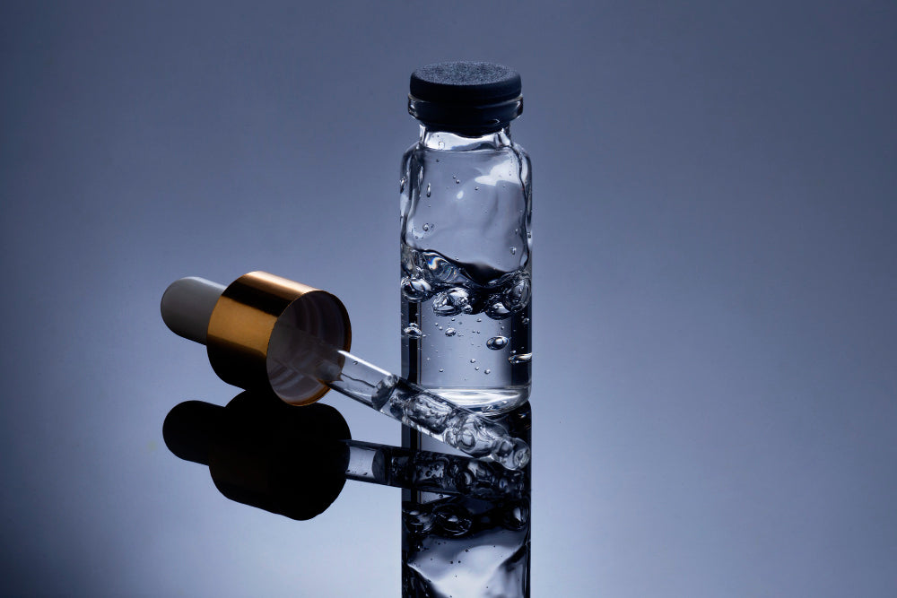 Transparente Glasflasche mit Pipette auf reflektierendem Untergrund